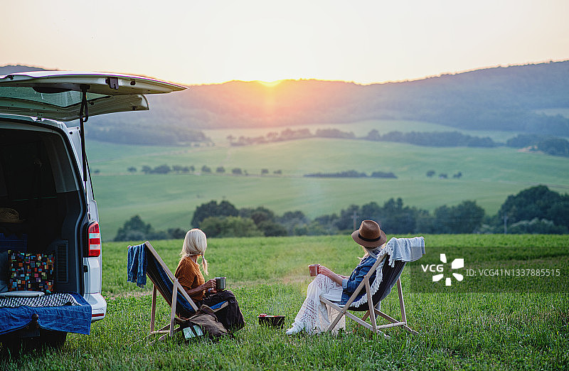 日落时分，老年妇女朋友在车旁吃东西的背影，房车旅行假日图片素材