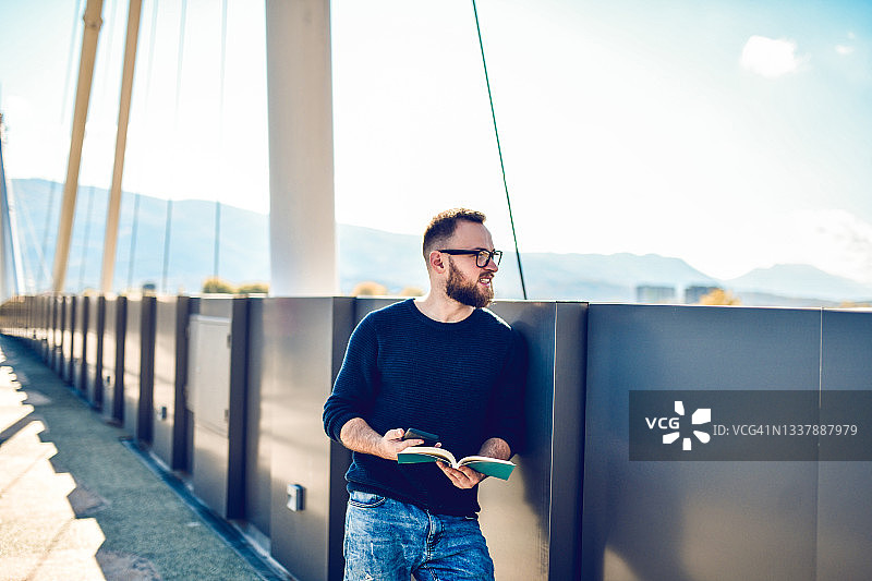 络腮胡男人在户外桥上沉思人生，阅读好书图片素材