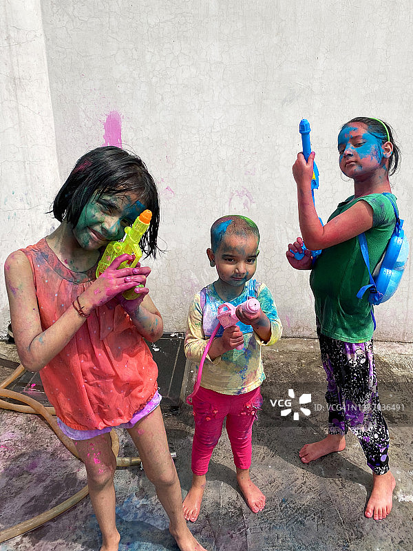 三个印度女孩在洒红节上玩耍，手持水枪，身上沾满彩色颜料图片素材