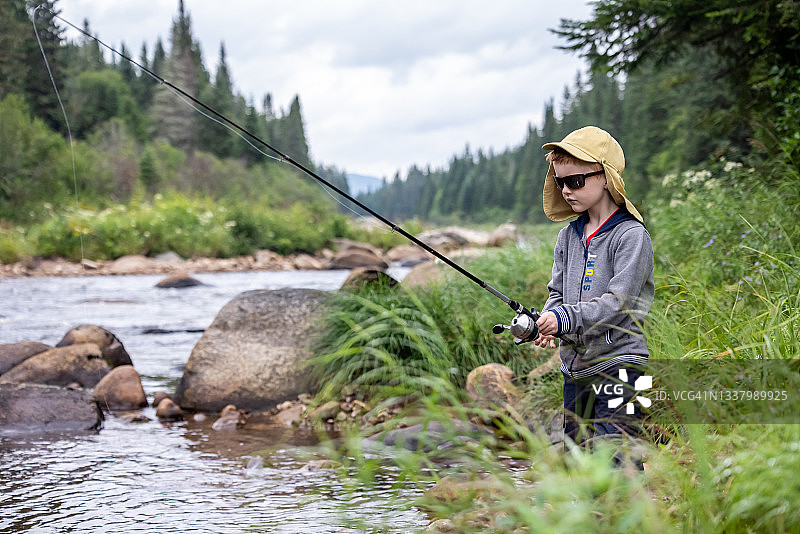 在魁北克河里钓鱼的可爱红发男孩图片素材