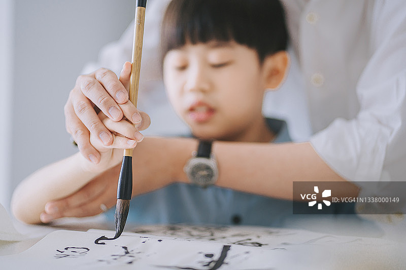 华人父亲手把手教儿子在家练习中国书法图片素材