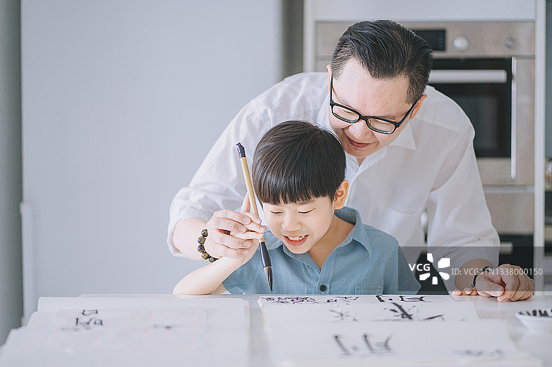 华人父亲手把手教儿子在家练习中国书法图片素材