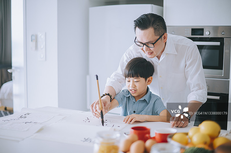 华人父亲手把手教儿子在家练习中国书法图片素材
