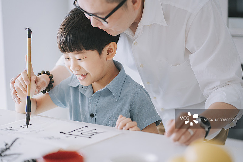 华人父亲手把手教儿子在家练习中国书法图片素材