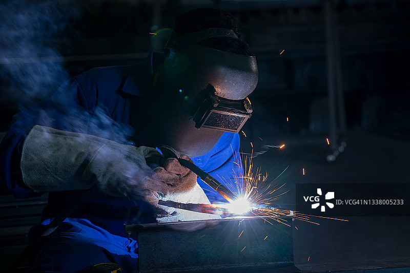 工厂工人在车间使用焊接机焊接金属，蓝色焊接火花，气体燃烧和蓝色烟雾图片素材