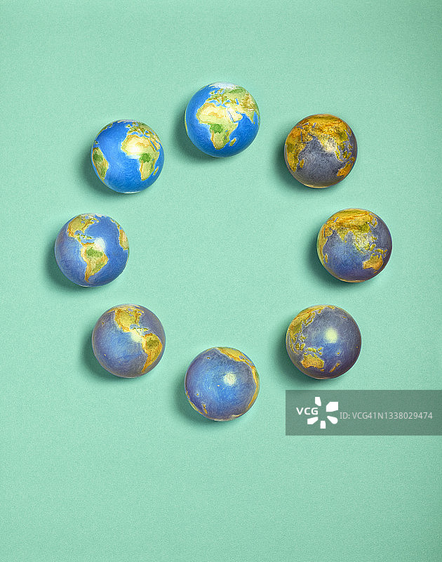 一群地球仪在绿色纸背景上呈圆形排列，地球仪从受污染到清洁逐渐变化（从一点钟方向顺时针排列）图片素材