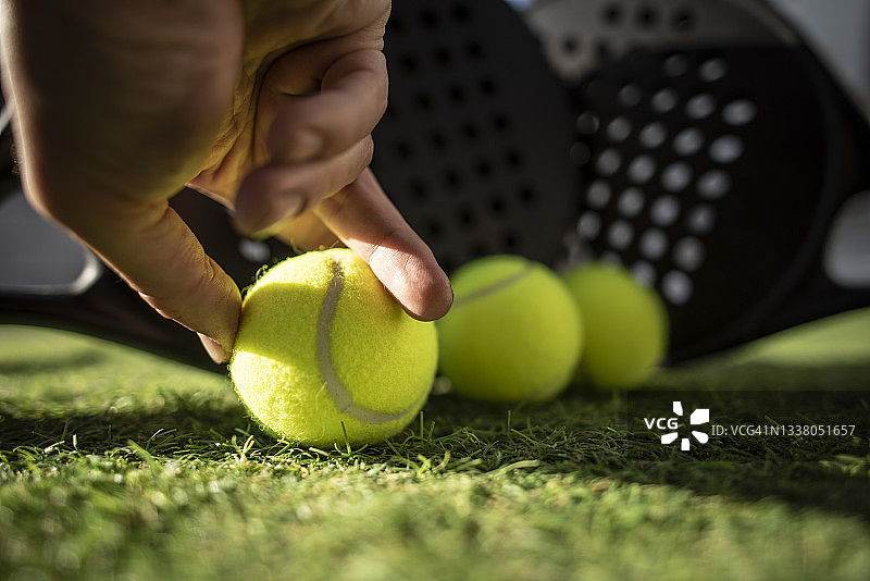 草地上的桨板网球拍和球，一只手捡起一个球图片素材