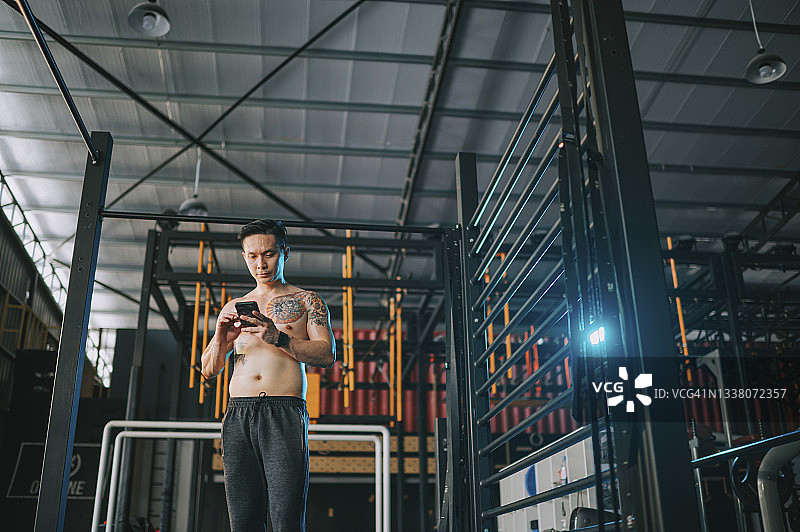 极限运动：在健身房练习街头健身前查看短信的亚洲健壮男性运动员图片素材