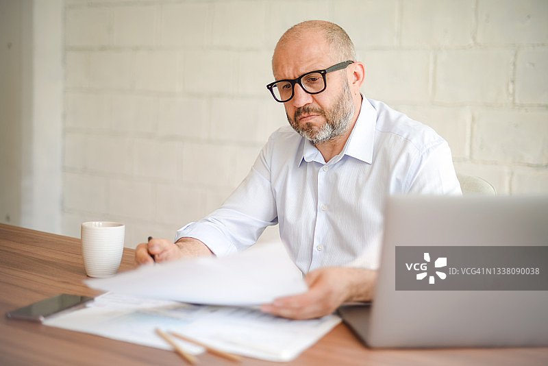 在办公室工作的成熟男人（使用笔记本电脑，处理文书工作）图片素材