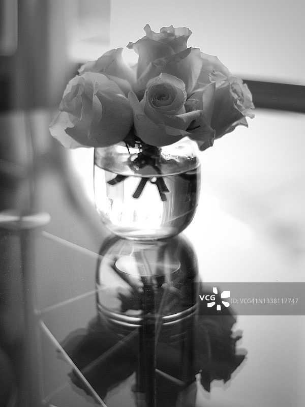 玻璃桌上玻璃花瓶中的白色玫瑰摆件竖版背景图片素材