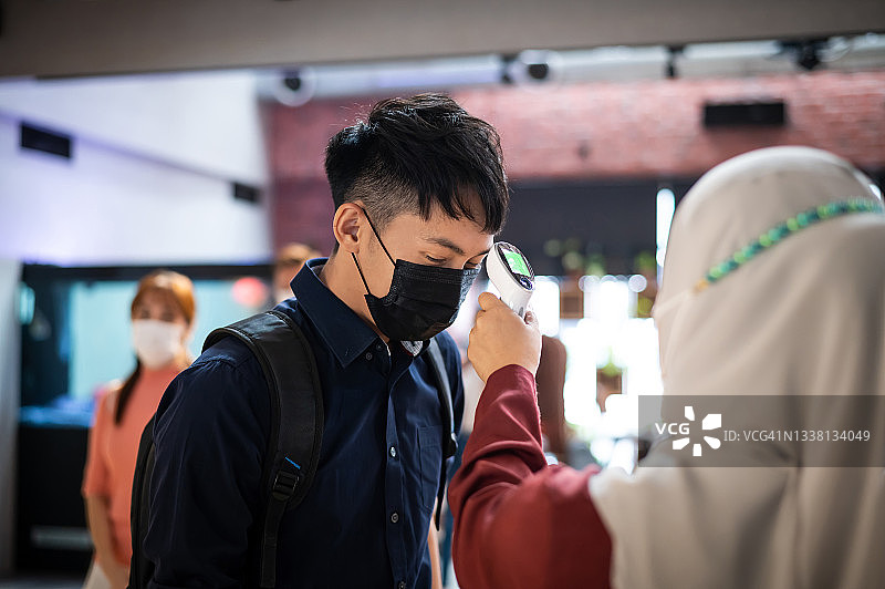 在大流行期间，戴着口罩给同事测量体温的上班族正在返回办公室上班图片素材