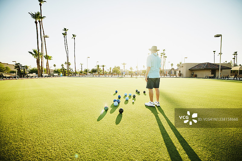 在夏天晚上草地保龄球比赛期间，男子观看伙伴保龄球比赛的宽镜头图片素材