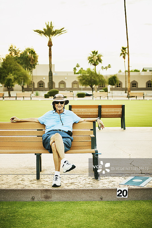 夏季傍晚草地滚球比赛后，老年男子在长椅上放松图片素材
