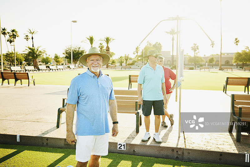 微笑的老年朋友准备在夏日傍晚进行草地保龄球比赛图片素材