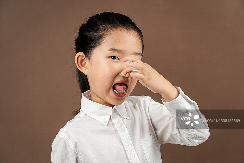 棕色背景下捏鼻子的小女孩图片素材