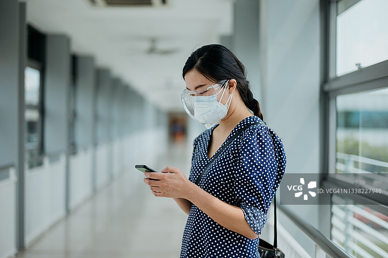 戴口罩和防护罩的亚洲女商人在人行道上使用智能手机图片素材