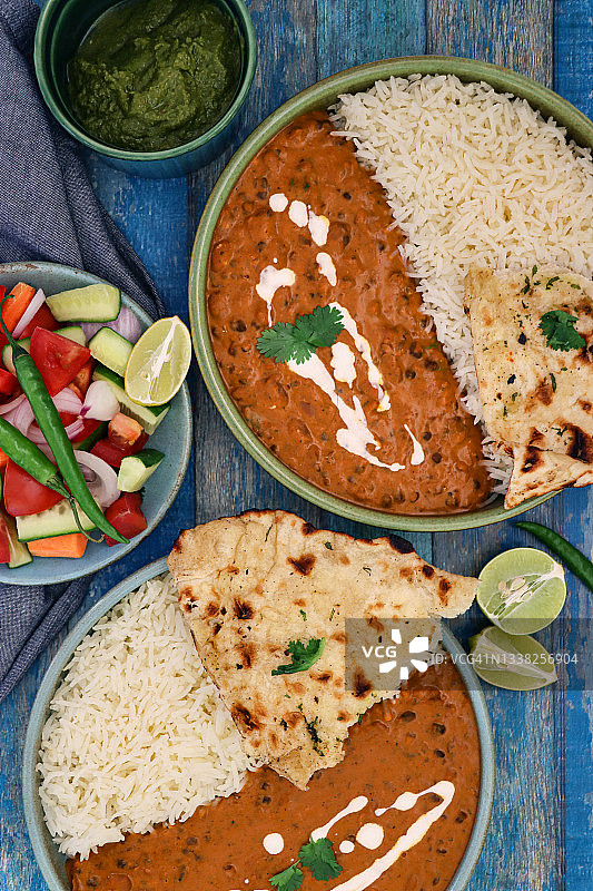 蓝碗自制奶油达尔（黑扁豆红腰豆咖喱）套餐，搭配白米饭、馕饼、柠檬片、青辣椒、沙拉、薄荷香菜酸辣酱，蓝色木纹背景图片素材
