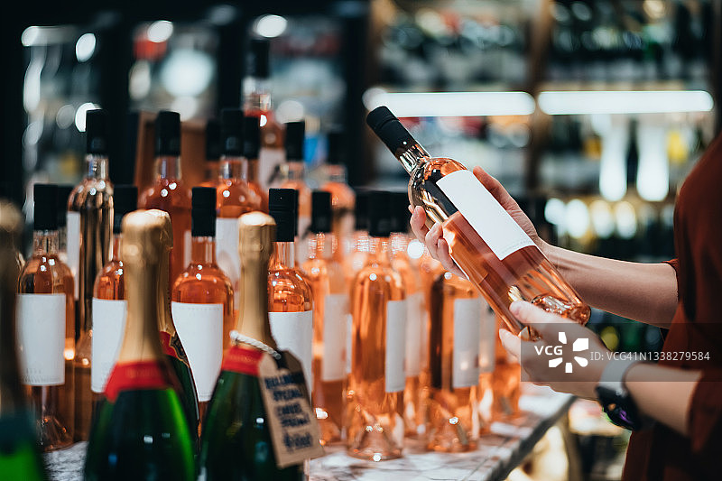 年轻亚洲女性在超市的酒类区挑选一瓶桃红葡萄酒图片素材