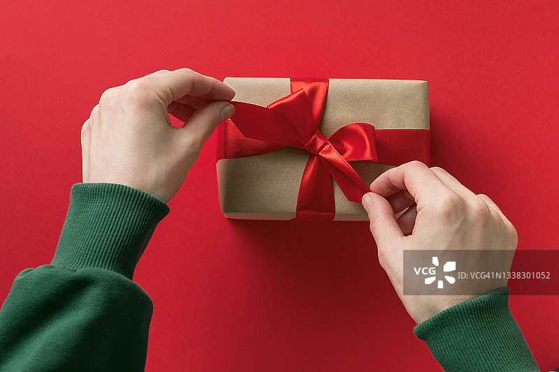穿着绿色毛衣的女孩在红色背景下拿着一个系着明亮丝带的精美礼品盒。圣诞节快乐概念图片素材