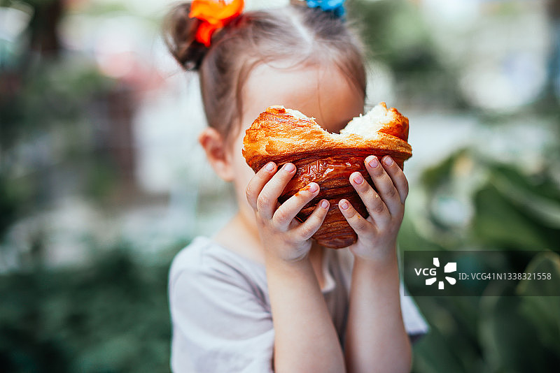 在街上户外吃酥脆羊角面包的金发小女孩图片素材