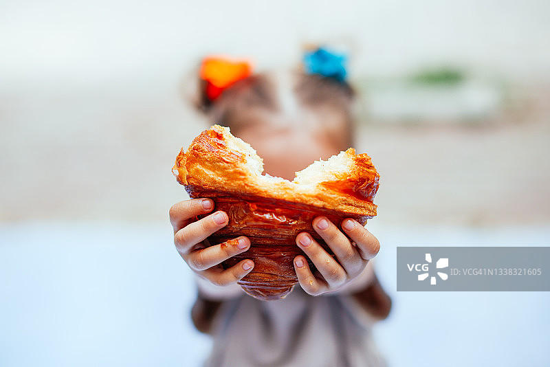 在街上户外吃酥脆羊角面包的金发小女孩图片素材