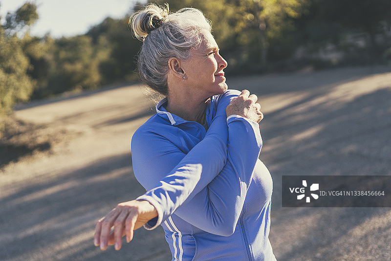 在阳光明媚的日子里，锻炼前伸展的中年妇女图片素材