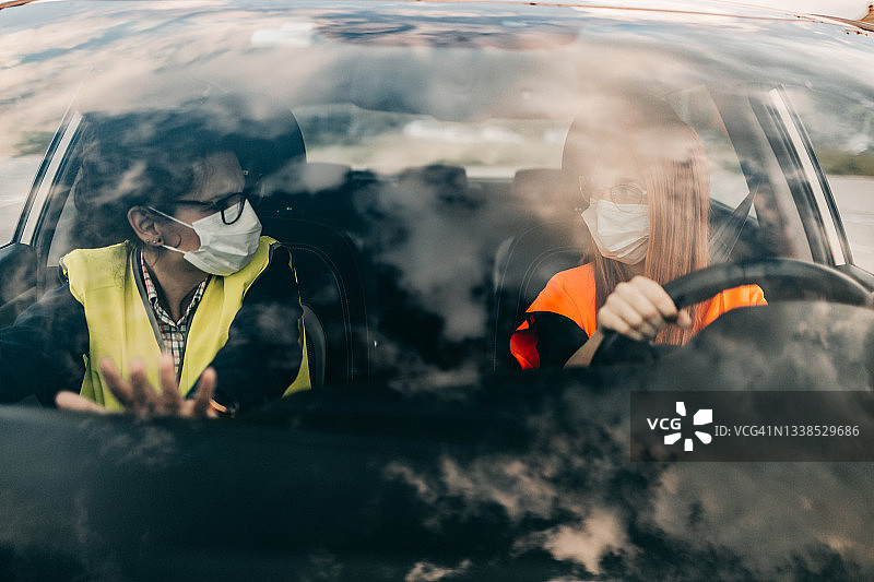 驾校或考试。美丽的年轻女人和她的教练一起学习如何开车。图片素材