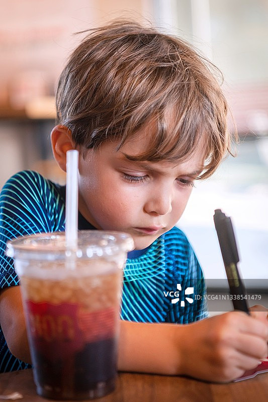 小男孩坐在学校餐厅里写作图片素材