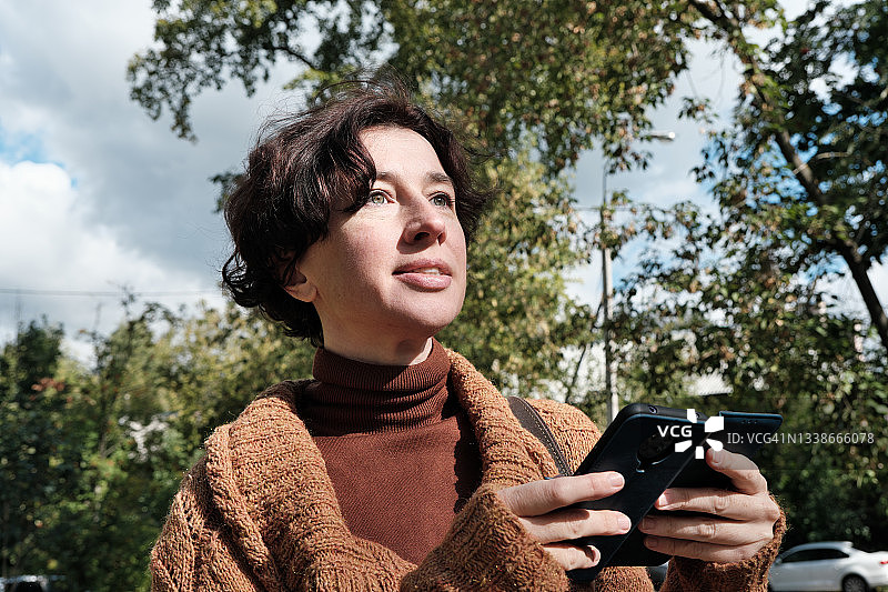 在秋日小镇街道上用手机的中年妇女上半身肖像图片素材