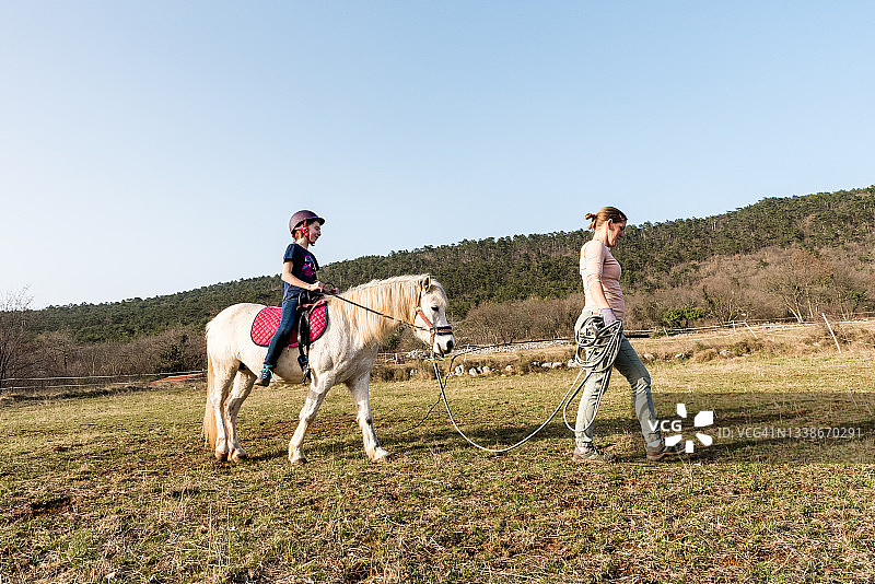 年轻女孩在冬季牧场上与教练一起训练骑马图片素材