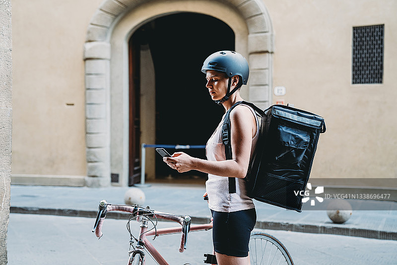 年轻送餐员骑自行车在门旁等候送餐，查看智能手机图片素材
