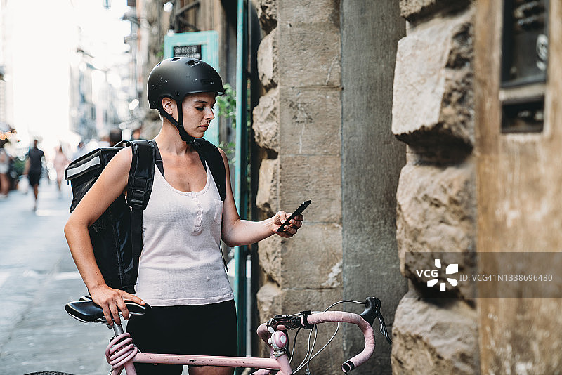 年轻送餐员骑自行车在门旁等候送餐，查看智能手机图片素材