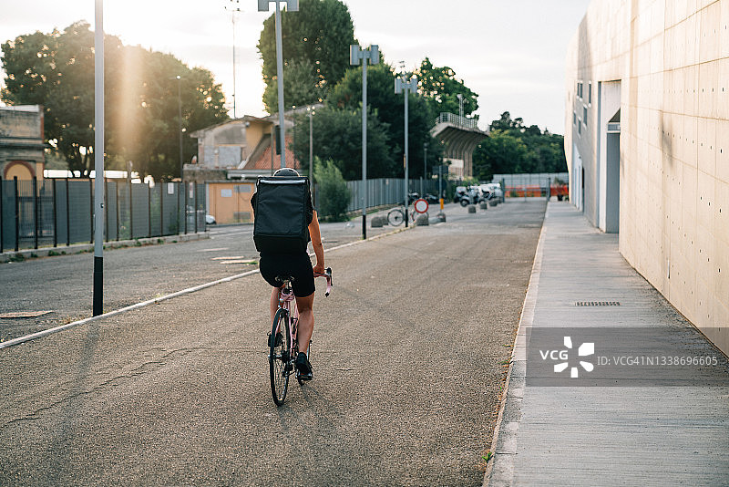 年轻外卖员在日落时骑自行车送餐图片素材