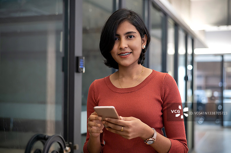 微笑的女商人用智能手机在现代办公室图片素材