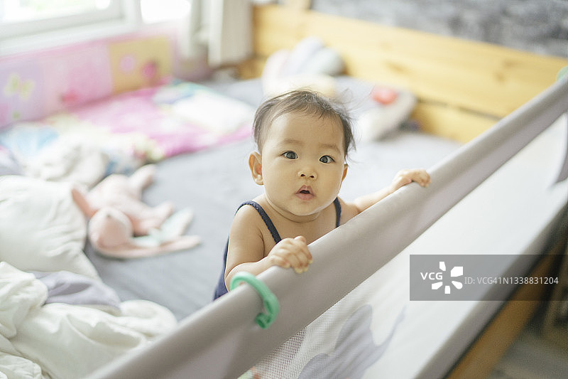 在卧室游戏围栏里站着的亚洲女婴图片素材