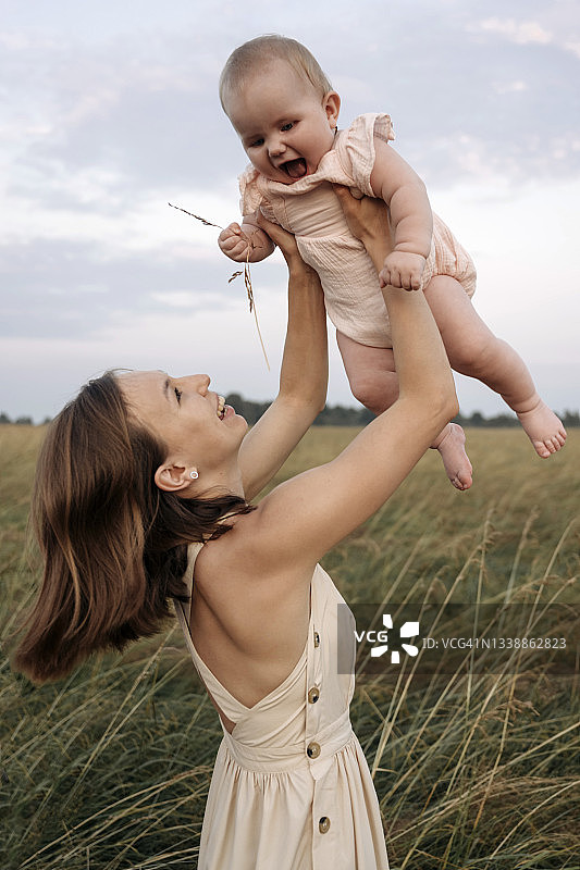快乐的年轻母亲在田野里和幼儿女孩玩耍图片素材