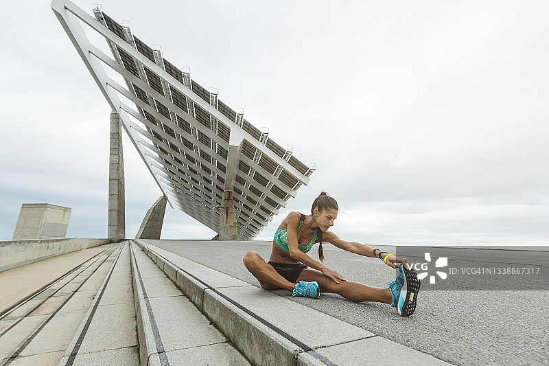 女运动员坐在人行道上伸展腿部图片素材