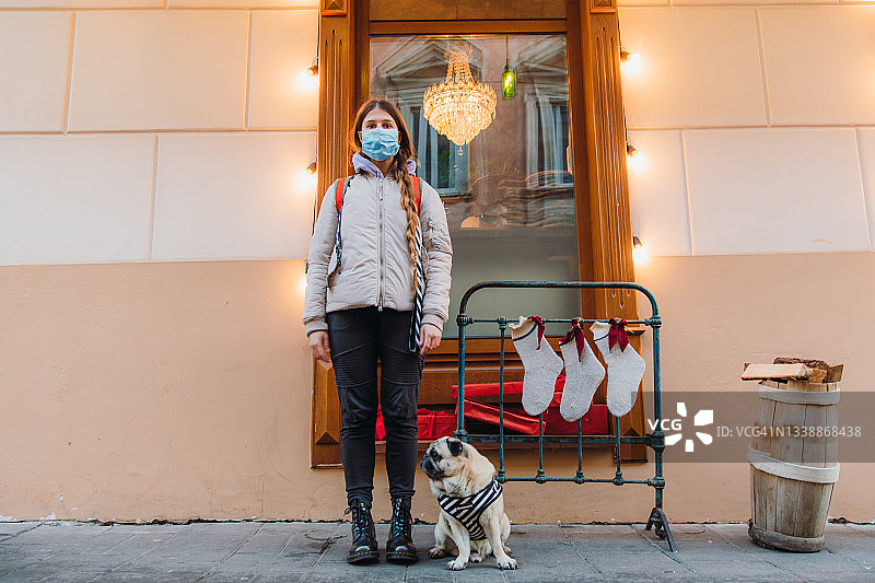 戴着口罩的年轻女人和一只狗在圣诞城市享受冬季时光图片素材