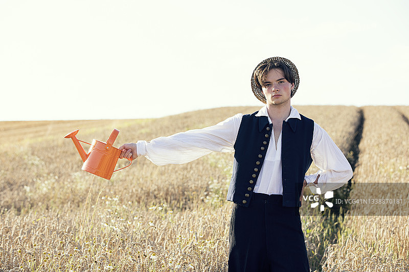 阳光明媚的日子里，青少年男孩在田野里拿着喷壶图片素材