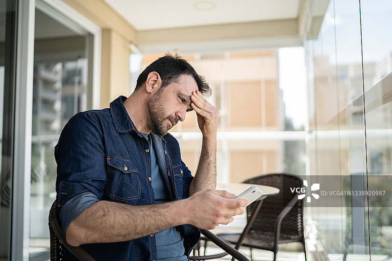 忧心忡忡的男子在公寓阳台上使用智能手机图片素材