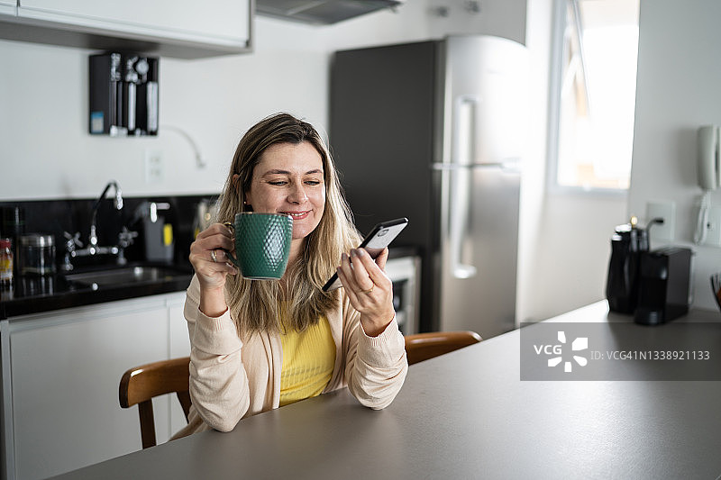 女人在家喝咖啡时用智能手机发送语音消息图片素材