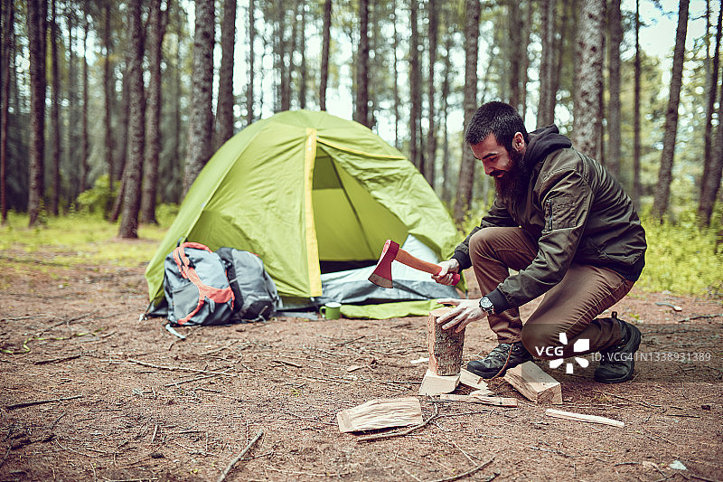 在帐篷旁劈柴的男露营者图片素材
