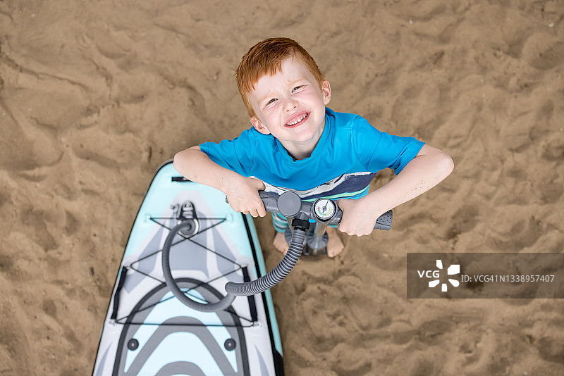 在魁北克夏季海滩给桨板SUP充气的可爱红发男孩图片素材