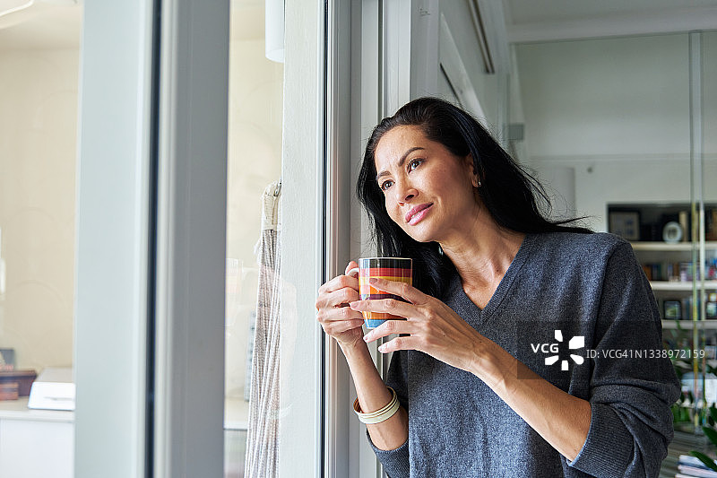 亚洲女子站在玻璃门旁，手持咖啡或茶杯图片素材
