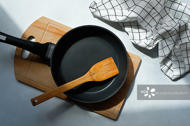 全新的干净的空铸铁煎锅和木制锅铲，放在砧板上。餐厅和咖啡馆、家庭厨房的烹饪理念。自己烹饪，参加烹饪美味佳肴的课程。图片素材