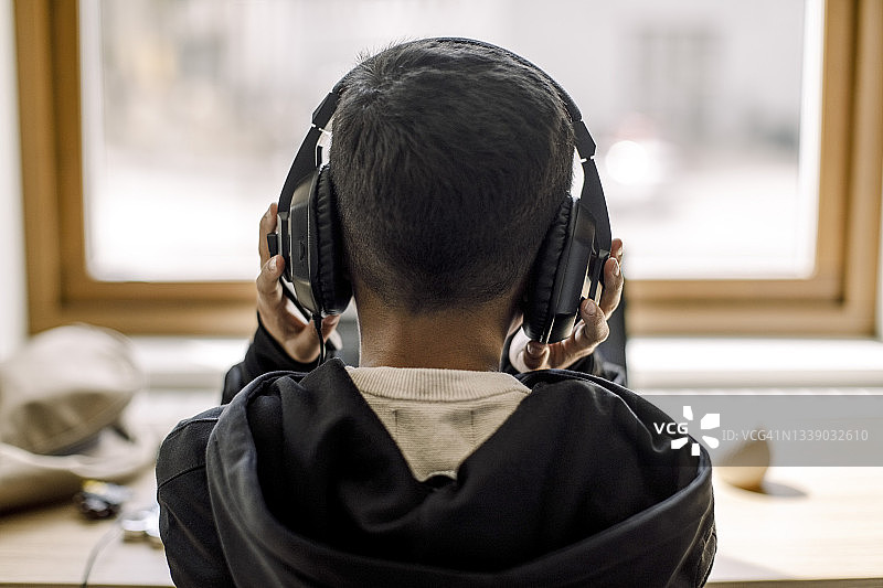 自闭症男孩戴着耳机在家的背影图片素材