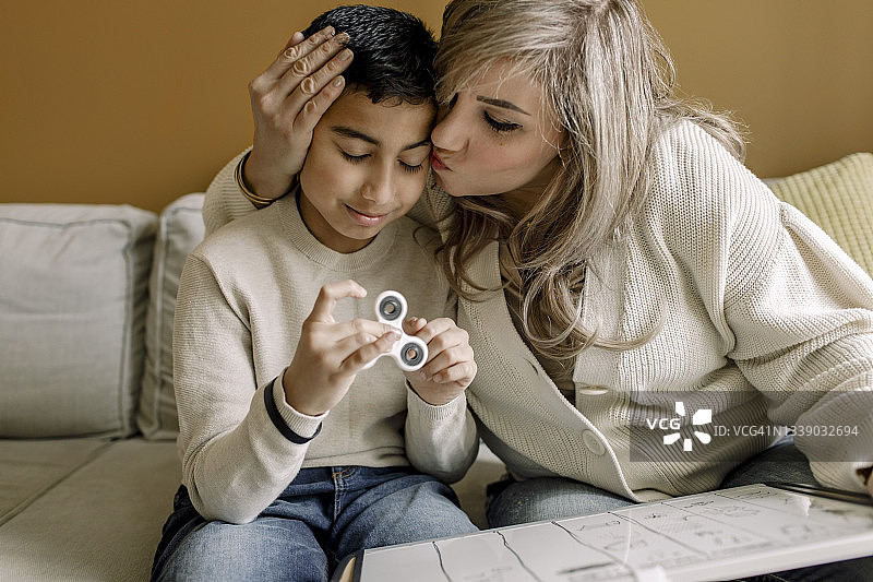 母亲在家辅导儿子功课时亲吻他，儿子患有ADHD和自闭症，用感官玩具帮助集中注意力图片素材