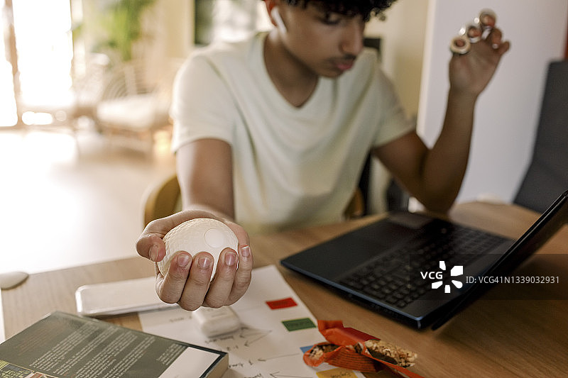 客厅里，自闭症少年坐在笔记本电脑旁抱着球图片素材