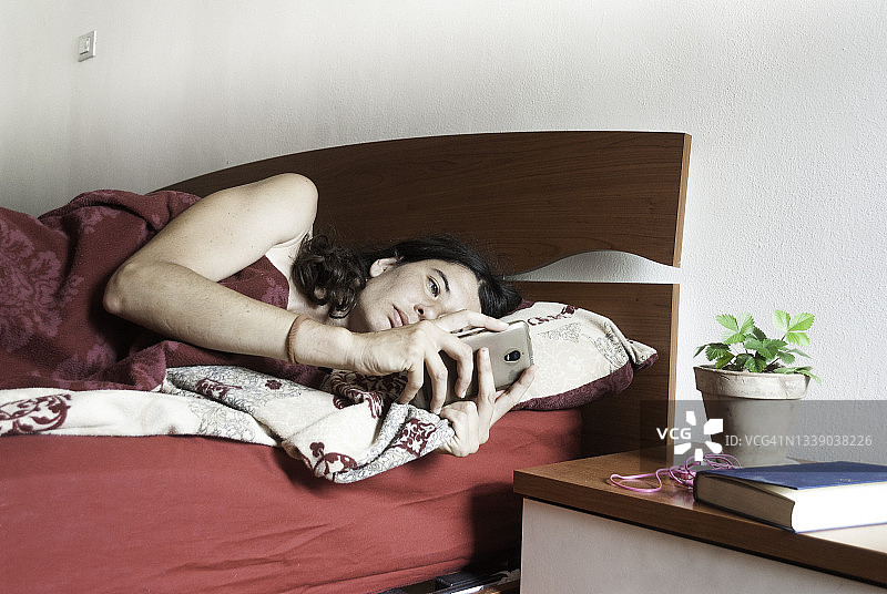 在卧室用智能手机的年轻女人。居家生活。图片素材