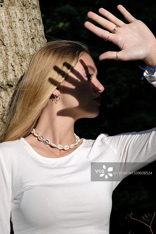 站在树旁，手放在脸前的少女，法国图片素材